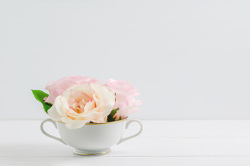 Artificial pink pastel rose flowers at white cup