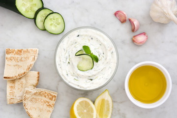 Tzatziki in bowl and ingredients on white marble
