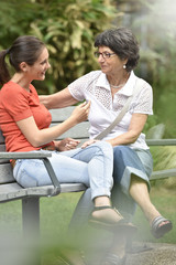 Senior woman with carer sitting on bench at the park