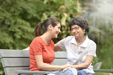 Fototapeta premium Senior woman with carer sitting on bench at the park