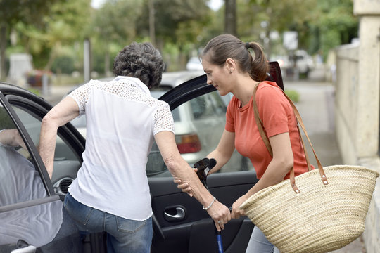 Young carer helping senior woman getting in car