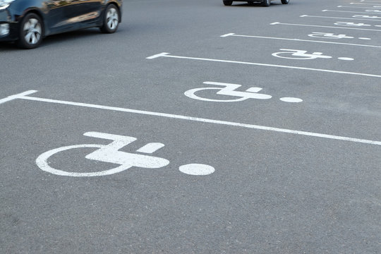 Empty parking places with handicapped or disabled signs on asphalt and detail of moving cars