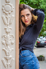 Young cute girl with long hair in a shirt and denim shorts walking in the park in Lviv Striysky sunny summer day posing near the columns at the entrance