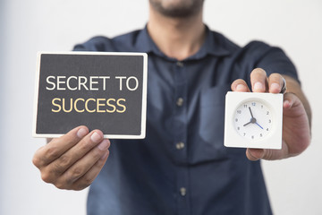 man holding chalkboard and clock with SECRET TO SUCCESS message,