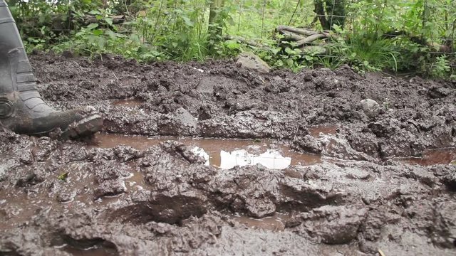 Adult male wearing wellington boots on extremely muddy ground.