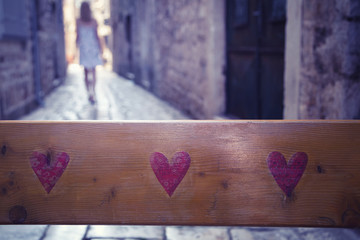 Lovely red hearts shapes on wooden background with blurry sad woman leaving the street. Conceptual relationship trouble background. Selective focus used.
