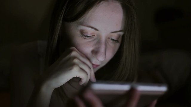 Young woman searching internet when lying on bed at home at night