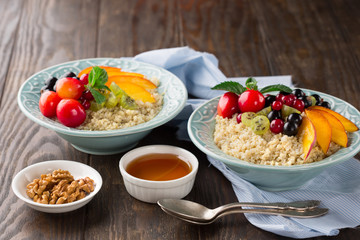 Healthy Quinoa porridge in a bowls with fresh fruits, nuts and agave syrup on rustic wooden background, selective focus