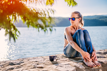 Woman sitting on a stone dock and drinking coffee