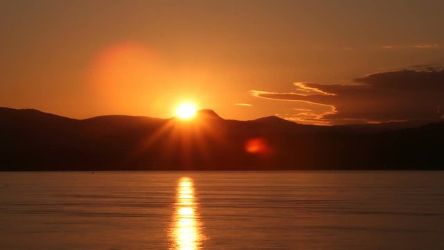 Time Lapse of the Sun behind low mountains with the ocean in the forground.