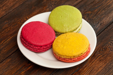 Three traditional french colorful macarons on plate, wooden background