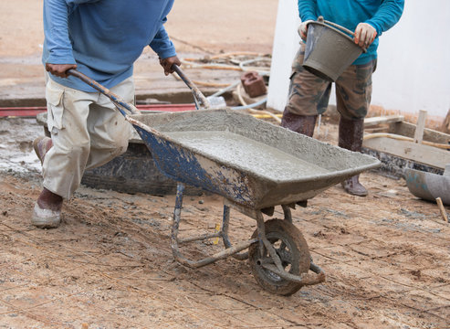 worker pushing barrow with wet cement to pouring concrete floor