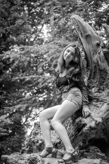 Young beautiful teenager girl with long hair in a shirt and denim shorts resting on a tree during a walk in the park Striysky in Lviv hot sunny summer day among the bushes and trees leaves
