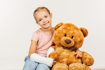 Young girl with broken arm is sitting and holding a soft toy bea