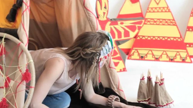 Young blonde girl in native American Indian costume crawling from wigwam