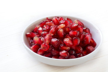 seeds of pomegranate in a small bowl on a white painted wooden background