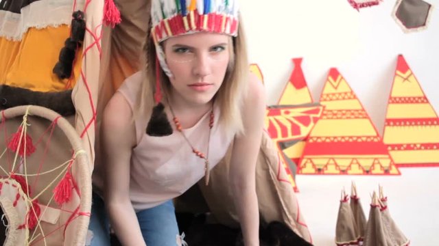 Young blonde girl in native American Indian costume crawling from wigwam