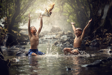 Boys playing with their duck in the creek - obrazy, fototapety, plakaty