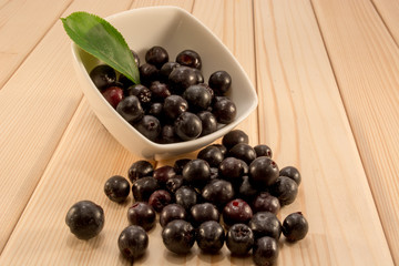 Bowl full of aronia spilled on wooden table
