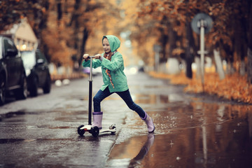 girl on scooter rides through the puddles