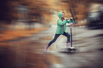 girl on scooter rides through the puddles