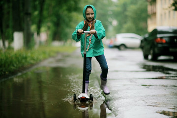 girl on scooter rides through the puddles