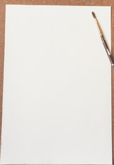White drawing paper and paint brush on brown background.