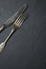 Antique silver knife and fork on a rustic slate background forming a page border