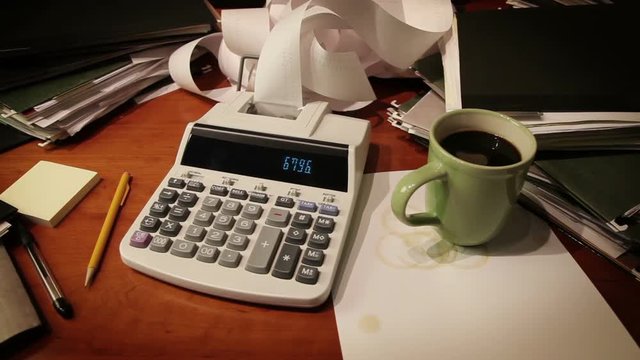 Dolly shot of a messy desk covered in paperwork.