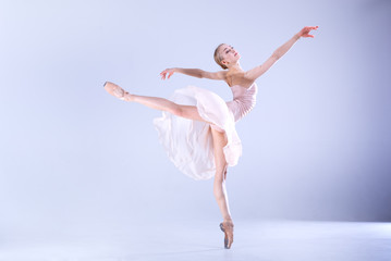 Ballet Perfection. Young and beautiful ballerina is dancing in a white studio full of light.