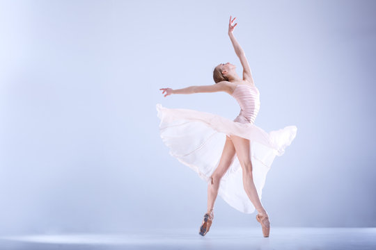 Ballet Perfection. Young and beautiful ballerina in a white dress is posing in a white studio full of light.