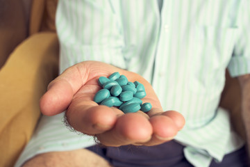 old man with a pile of blue pills in his hand - obrazy, fototapety, plakaty