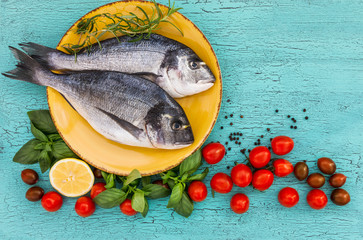 Raw dorado fish on yellow plate, tomatoes, basil and lemon. Top view, copy space 