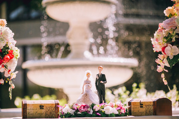 wedding bride and groom couple doll on lace table on the background of the fountain outdoor.