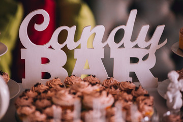Delicious wedding reception candy bar dessert table. Word "Candy bar" made of wood and white color. Delicious sweet buffet with cupcakes, tiramisu glasses and other desserts