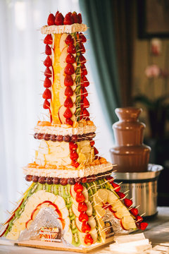 Friuit Eiffel tower for chocolate fountain fondue at candy bar. Stylish luxury decorated tables for the celebration for a wedding of happy couple, cathering in the restaurant.