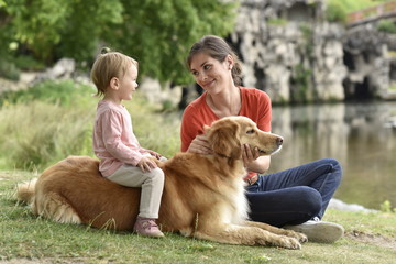 Woman and baby girl playing with golden retriever dog