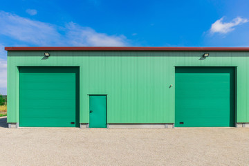 Front einer modernen Fabrikhalle in Grün mit 2 Rolltoren einer Tür und Außenbeleuchtung - Front...