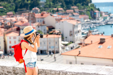 Young female traveler with red backpack photographing with photo camera Piran old town. Traveling...