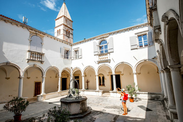 Young female traveler photographing with phone old monastery in Piran town. Traveling in Slovenia