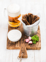 Beer snack set. Pint of pilsener in mug, open glass beer bottle, rye bread croutons with garlic cream cheese sauce served with fresh parsley and garlic on rustic wooden board over white painted old