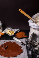 The process of baking chocolate cake base of shortcrust pastry. Working with dough at home kitchen. Ingredients for baking: eggs, flour, butter, sugar on black table and dark background.