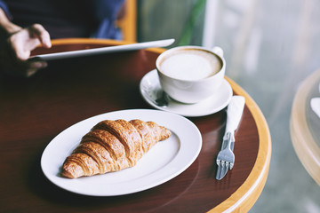 Fresh croissant and cappuccino on cafe table