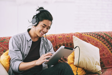 Cheerful guy listening to music in tablet computer
