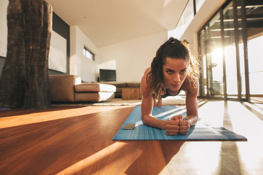 Fit young woman doing push ups at home - Powered by Adobe