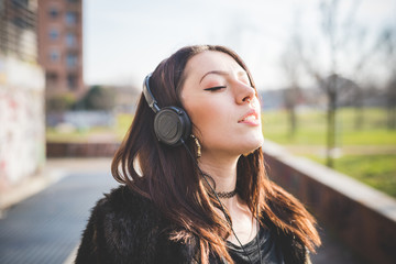 Young beautiful caucasian indie woman with septum piercing outdoor in the city listening music with headphones relaxing with eyes closed - music, relaxing, carefree concept