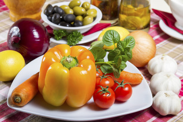 Fresh, orange bell pepper, basil, cherry tomatoes and carrot served on a plate; next to the bowl with green and black olives, onion, garlic - vegetable, herb, curative, vegan food.