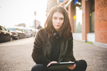 Young beautiful caucasian indie woman with septum piercing using tablet outdoor in city back light, looking at camera smiling - serene, technology, social network concept