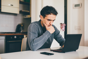 Naklejka premium Young handsome caucasian brown hair man sitting at the table tapping on the keyboard of a notebook – business, communication, social network concep