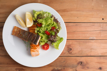 Grill salmon steak serve with lemon and colorful salad on wooden table top view